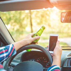 Driver holding a beer bottle and phone, illustrating DWI Arrest - Law Office of Ira Z. Miller