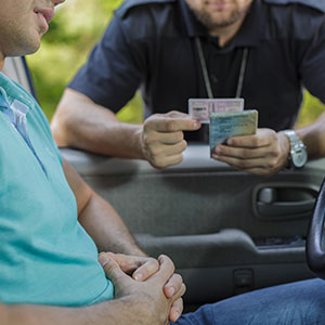 Police officer examining a driver's license during a DWI stop, indicating suspension risk - Law Office of Ira Z. Mill