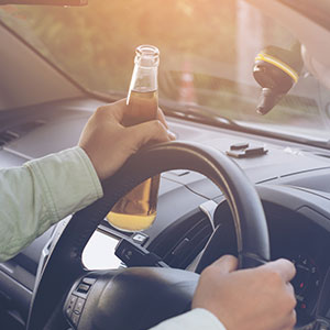 Driver holding a beer bottle, illustrating risks of Driving While Intoxicated in Texas - Law Office of Ira Z. Miller