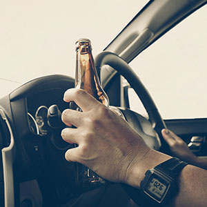 Hand holding a beer bottle while driving, highlighting DWI vs. DUI issues in Texas - Law Office of Ira Z. Miller